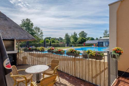 a patio with a table and chairs and a fence with a pool at Het Familie Boshuisje - vakantiewoning op prachtig park met veel faciliteiten inc ligbad in Gramsbergen