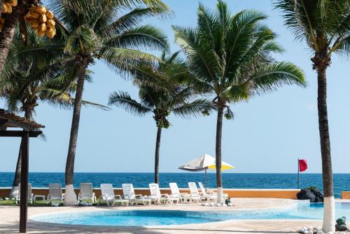 a swimming pool with palm trees and the ocean at Hotel Cayman Suites in Monterrico