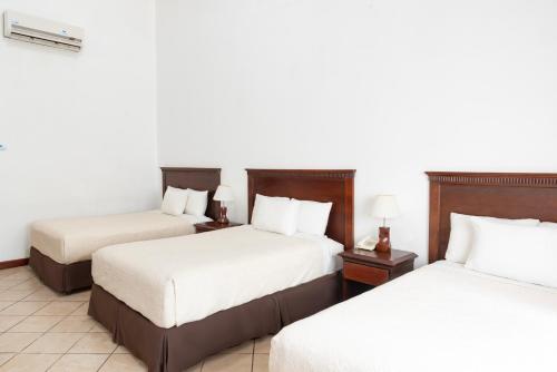 two beds in a hotel room with white walls at Hotel Cayman Suites in Monterrico
