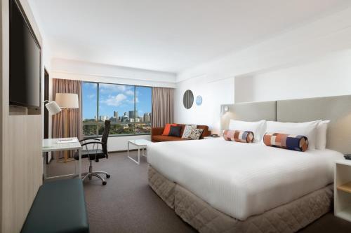 ein Hotelzimmer mit einem großen Bett und einem Schreibtisch in der Unterkunft Rydges Parramatta in Sydney