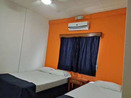 Habitación con 2 camas y pared de color naranja. en Hotel Mango Cafe, en Tela