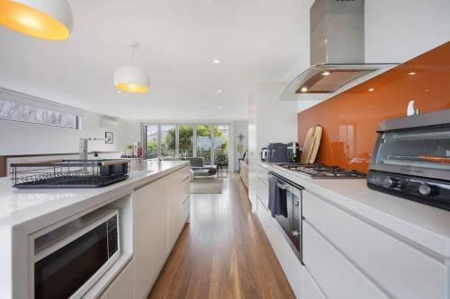 a large kitchen with white counters and an orange wall at Silver Ball Retreat in Warrnambool