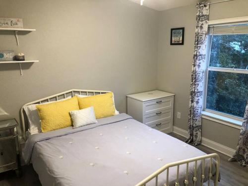 a bedroom with a bed with yellow pillows and a window at Swansea-by-the-Sea -- Spacious home - heated pool, hot tub, walk to beach! in Ormond Beach