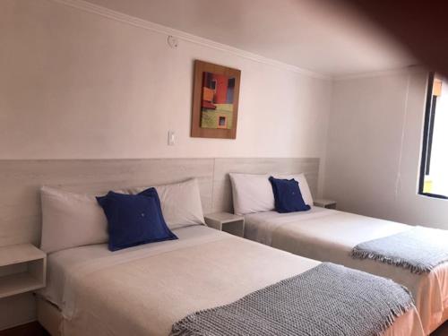 2 camas en una habitación blanca con almohadas azules en Hotel Mediterraneo Quito, en Quito
