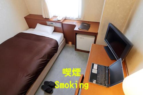 a small room with a bed and a desk with a computer at Utazu Grand Hotel in Utazu