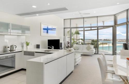 a kitchen with white cabinets and a living room with a view at Monaco Caloundra in Caloundra