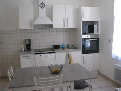 une cuisine avec des armoires blanches et une table avec des chaises dans l'établissement Maison la Soleiade, à Carcassonne