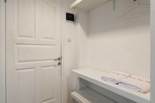 a white bathroom with a door and two towels on a shelf at Rumah Kayu Manis Bintaro in Jakarta
