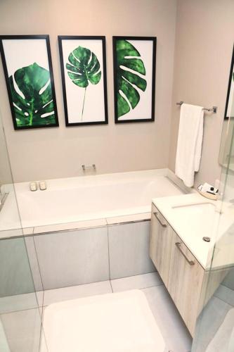 a bathroom with a tub and a sink and framed pictures at Menlyn Trilogy - 2 Bedroom & Great Views - No Loadshedding in Pretoria