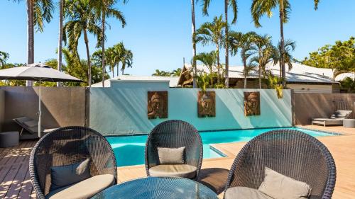 a patio with chairs and a pool with palm trees at The Pearle of Cable Beach in Broome