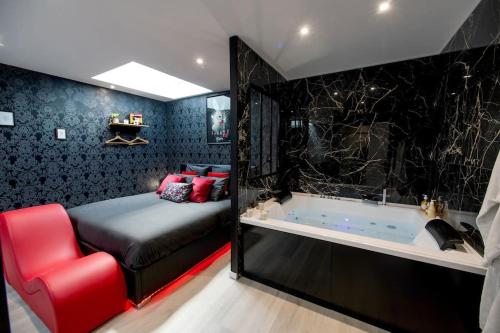 1 dormitorio con bañera, cama y silla roja en * Love Room jacuzzi *, en Aubie-et-Espessas