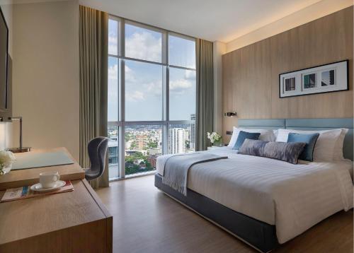 a bedroom with a bed and a desk and a large window at Somerset Sukhumvit Thonglor in Bangkok