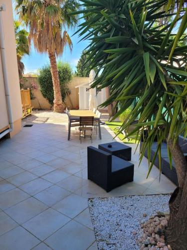 een patio met een tafel en stoelen en palmbomen bij Le petit coin de paradis in La Londe-les-Maures