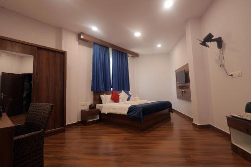 a bedroom with a bed with blue curtains and a television at MJ Avyanna Resort & Convention Centre, Bengaluru in Bengaluru