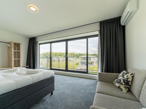 een slaapkamer met een bed en een bank en een groot raam bij 16p group accommodation in 2 villas on the water in Zeewolde