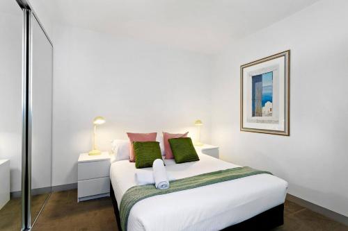 ein Schlafzimmer mit einem weißen Bett mit grünen und rosa Kissen in der Unterkunft Carlton Delight - Patio Abode near Queen Vic Market in Melbourne