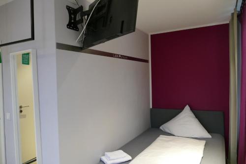 a small bed in a room with a purple wall at Pension Sölde UG in Dortmund