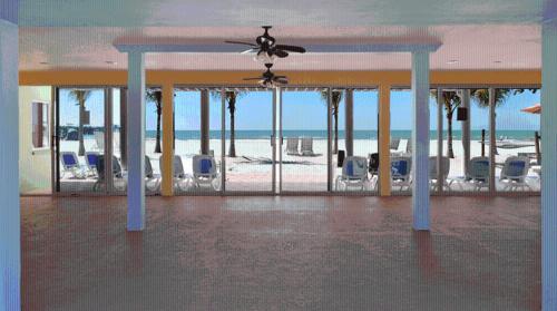 a room with a ceiling fan and chairs and the beach at Hotel SOL in St Pete Beach