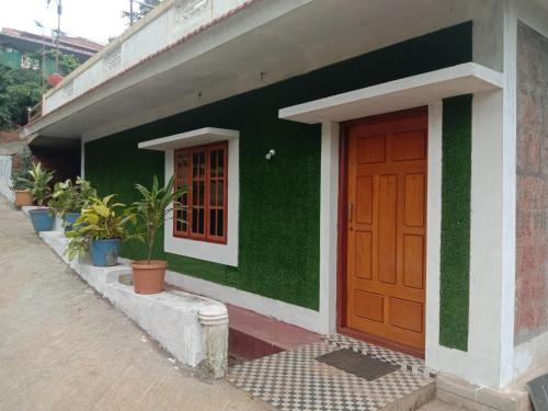 a green building with a brown door and potted plants at Shivalaya Homestay in Madikeri