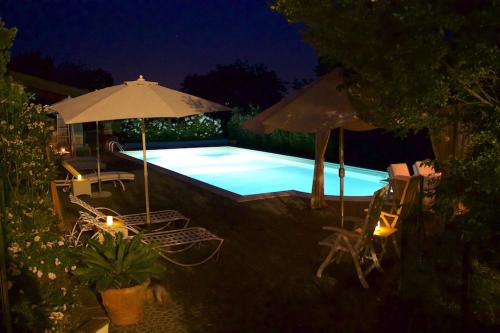 a swimming pool with chairs and an umbrella at night at Cascina Manu in Rosignano Monferrato