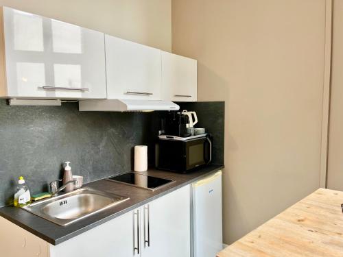 une cuisine avec des armoires blanches, un évier et un micro-ondes dans l'établissement Suite Orphelins 3 1er, à Reims