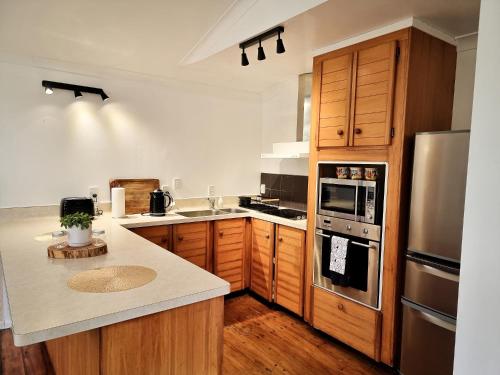 La cuisine est équipée d'armoires en bois et d'un réfrigérateur en acier inoxydable. dans l'établissement The Hidden Gem - tranquility close to town, à Wellington