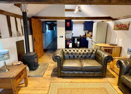 a living room with a leather couch and a stove at Stable Cottage at Lee Wick Farm Cottages & Glamping in Clacton-on-Sea