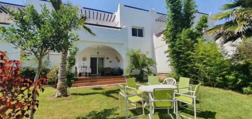 Casa blanca con mesa y sillas en el patio en La Vida Villa Alcudia Smir Fnideq, Holiday Homes, en Tetuán
