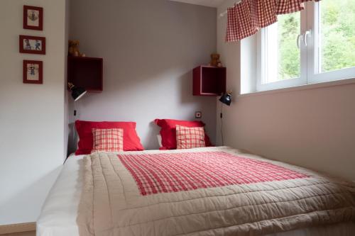 a bedroom with a bed with red pillows and two windows at A l Orée du Bois in Rimbach-près-Masevaux