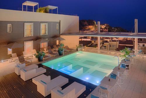 una piscina con sedie bianche e un edificio di NH Collection Taormina a Taormina