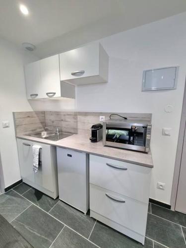 une cuisine avec des armoires blanches, un évier et un micro-ondes dans l'établissement Le Rio - Studio gare et centre, à Mulhouse