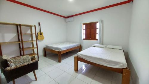 - une chambre avec un lit, une chaise et une guitare dans l'établissement Casa temporada em Prado-BA ótimo preço, à Prado