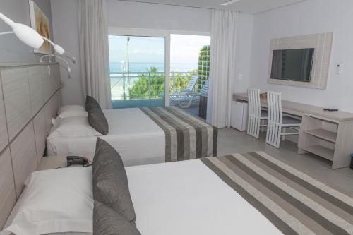 a hotel room with two beds and a desk and a window at Hotel Vicino al Mare in Guarujá