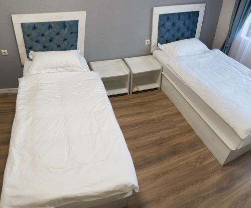 two beds in a room with white sheets at Khan Plaza in Almaty
