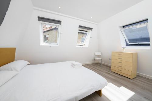 um quarto branco com uma cama e 2 janelas em Modern Apartment in South West London em Londres