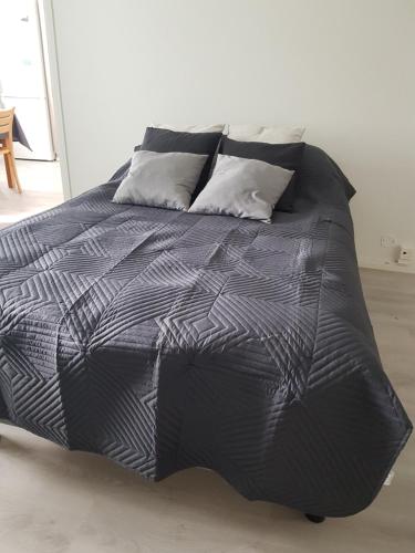 a bed with a black comforter and three pillows at Kaarteen yksiö in Oulu