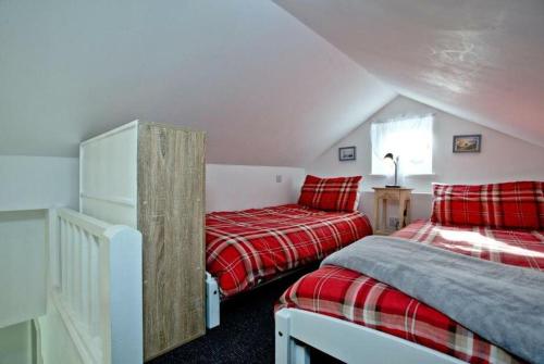 two beds in a attic bedroom with red plaid sheets at Hill Head Cottage in Saint Columb Major