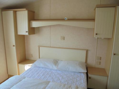 a bedroom with a bed with white sheets and cabinets at Golden Sands: Richmond GS:- 6 berth, Blow heated, Access to the beach in Ingoldmells