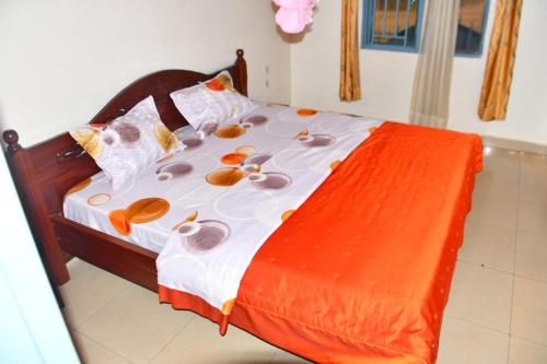 a bed with an orange and white comforter and pillows at Enchante Suites Kigali in Kigali