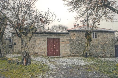 a stone house with a red door and two trees at Casa do Viñal 