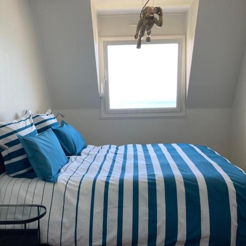 - un lit avec une couette à rayures bleue et blanche et une fenêtre dans l'établissement Appartement standing vue Mer, à Trouville-sur-Mer