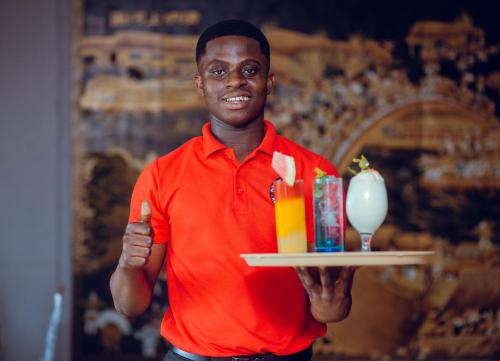 a man holding a tray with two drinks and a candle at Noble House Hotel in Kumasi