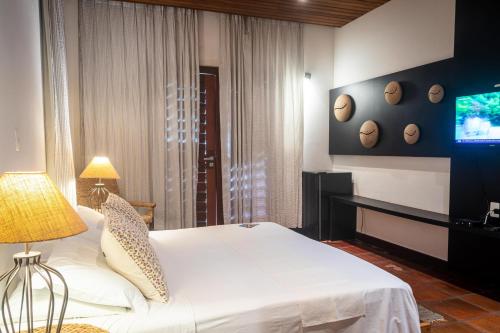 a bedroom with a white bed and a television at Hotel Villaggio Tudo Bom in Uruau