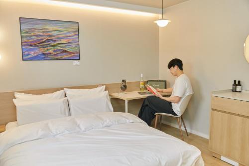 un hombre sentado en un escritorio junto a una cama en Aank Thepeak Hotel Incheon Songdo, en Incheon