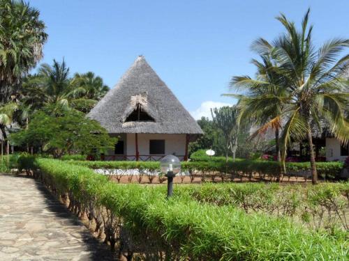 a house with a thatched roof and palm trees at Private cottages @ Karibuni Villas in Malindi