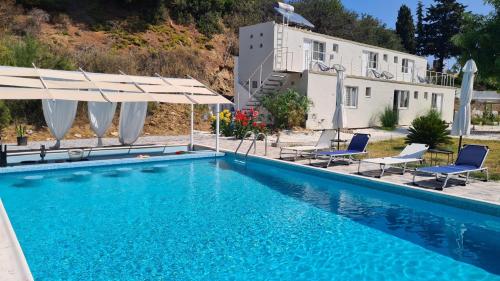 a pool with chairs and umbrellas in front of a house at Greco Paradise Suites - ADULT ONLY in Nea Skioni