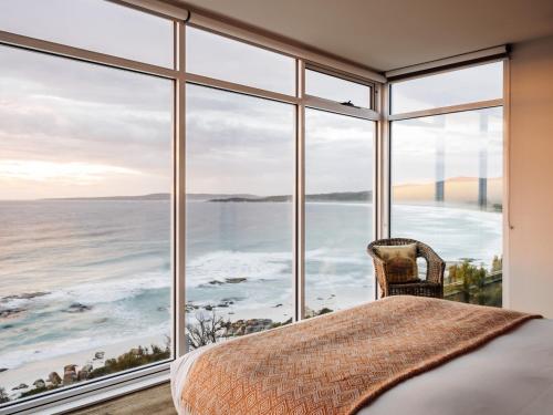 a bedroom with a large window view of the ocean at Holland House Bay of Fires in Binalong Bay