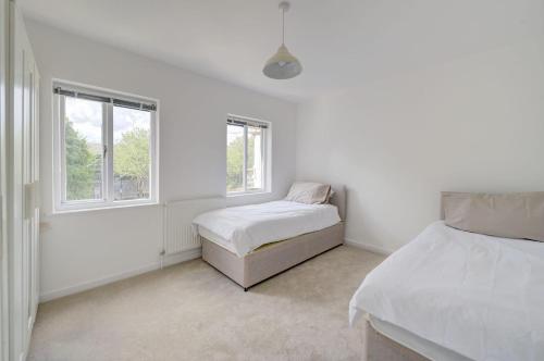 a white bedroom with two beds and two windows at Private house seconds from Portobello Road in London