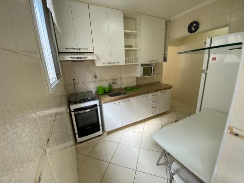 a small kitchen with white cabinets and a refrigerator at Pé na areia canto do forte II in Praia Grande