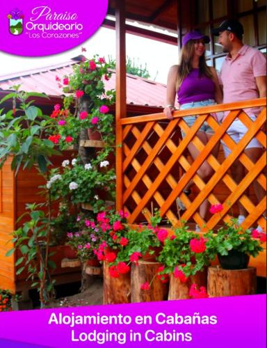 a man and woman standing on a balcony with flowers at Paraiso Orquideario in Baños